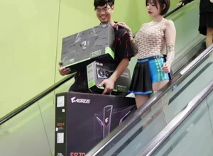 Мужчина и женщина спускаются по эскалатору с коробками компьютерной техники.