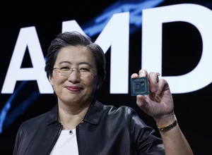 Женщина с короткой стрижкой и очками, улыбается, держит процессор на фоне логотипа AMD.