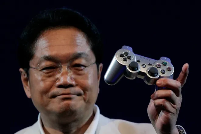 Человек в белом пиджаке держит в руке игровую консоль PlayStation.